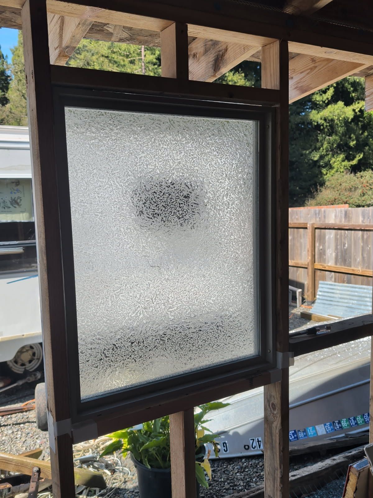 Frosted glass windowpane in a dark wooden frame mounted outdoors on a porch.