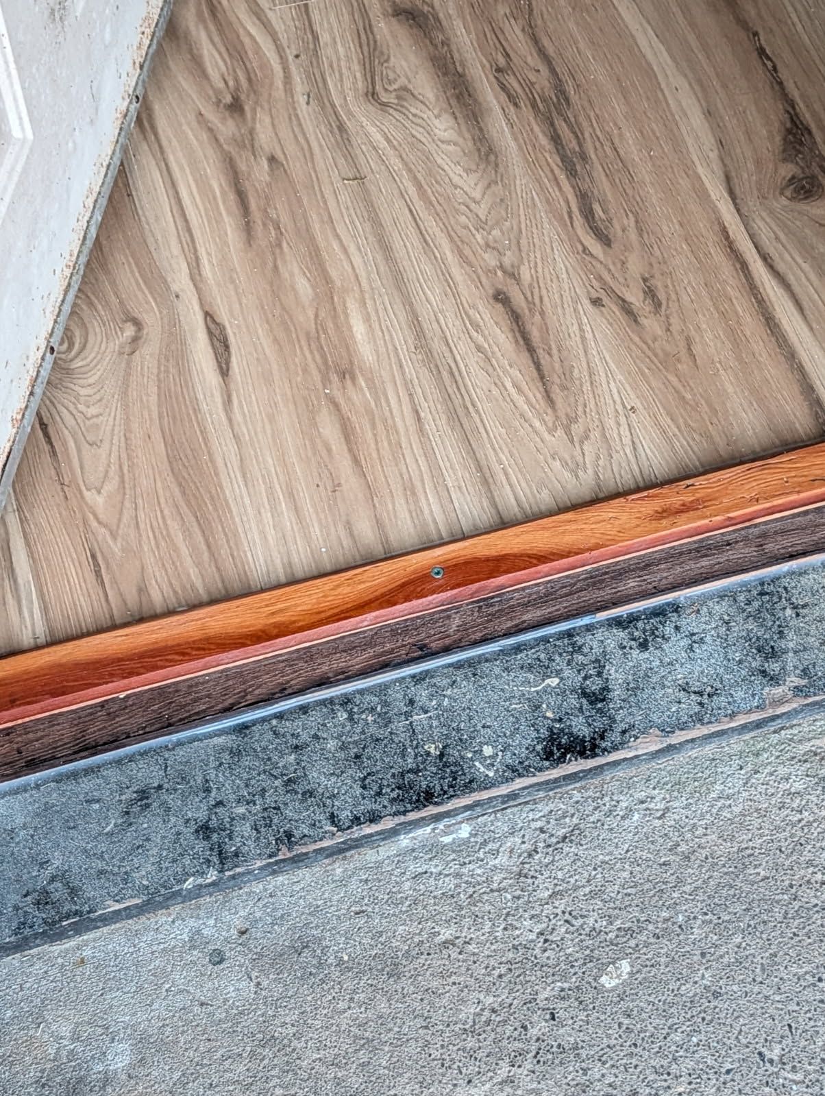 Wooden floor meeting a stone threshold at a doorway, with a white wall edge on the left