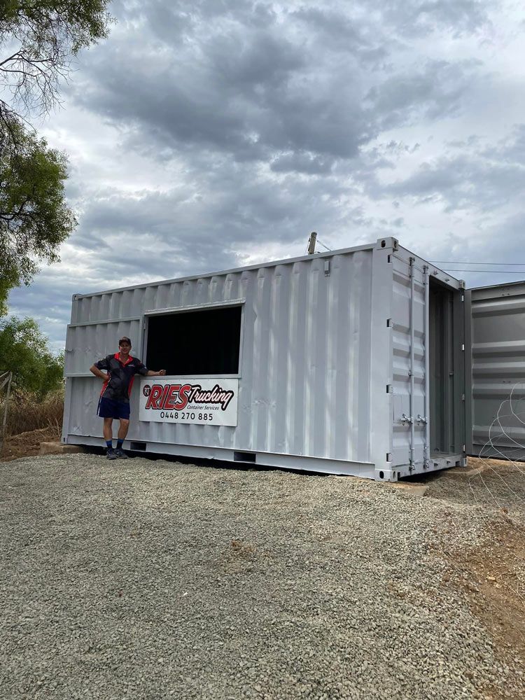 A Man Is Standing In Front Of A Shipping Container — Ries Trucking in Gowrie Mountain, QLD