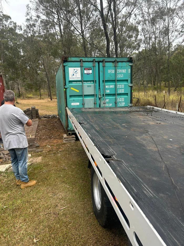 A Man Is Standing Next To A Green Shipping Container — Ries Trucking in Gowrie Mountain, QLD