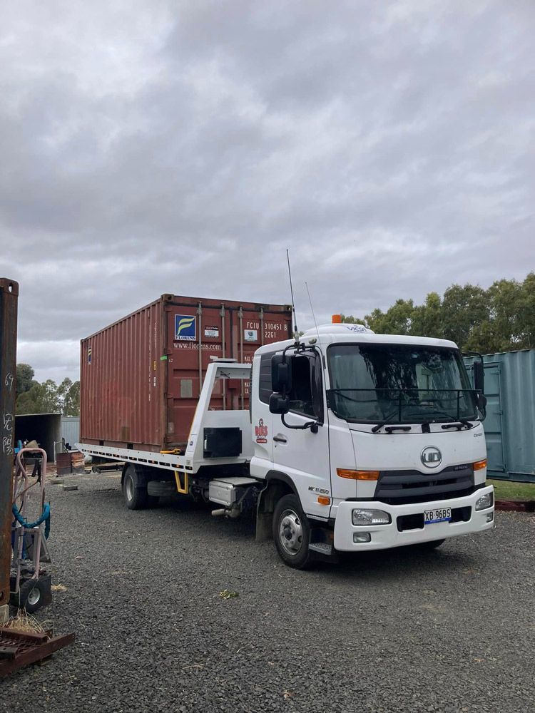 A Tow Truck With A Red Shipping Container on The Back Is Parked in A Gravel Lot — Ries Trucking in Gowrie Mountain, QLD