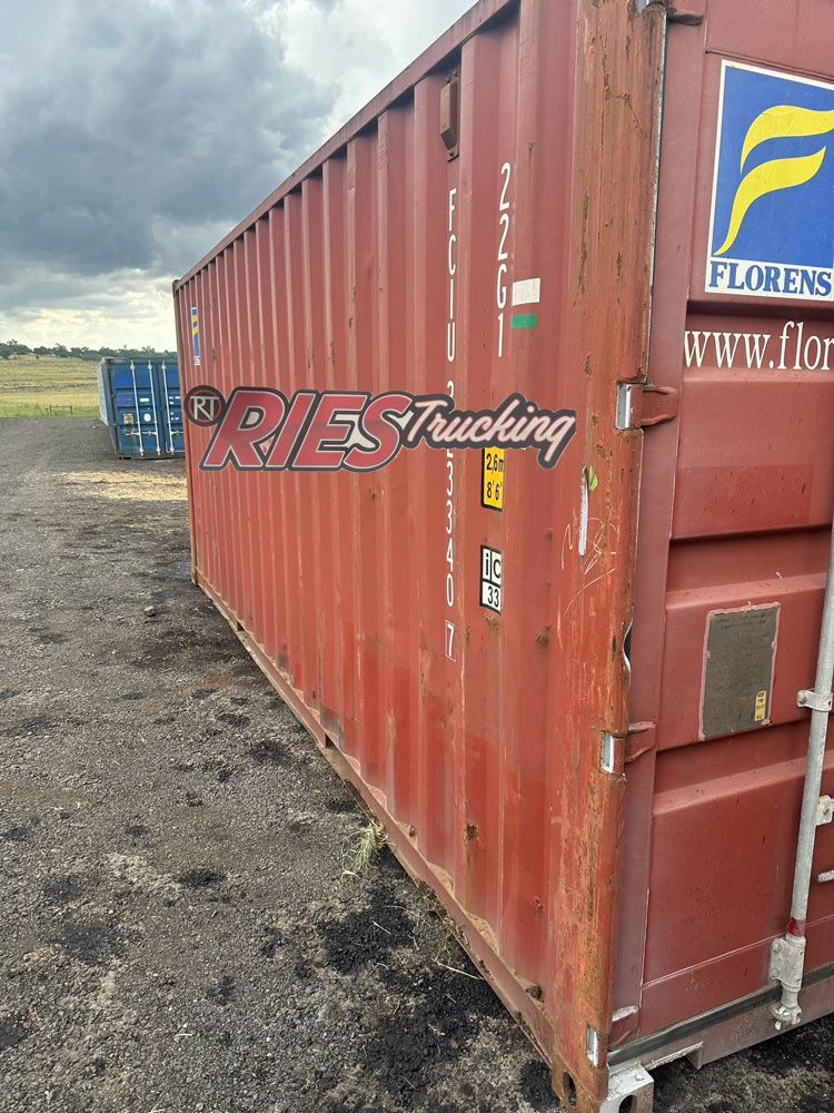 A Red Shipping Container Is Sitting In A Dirt Field — Ries Trucking in Gowrie Mountain, QLD