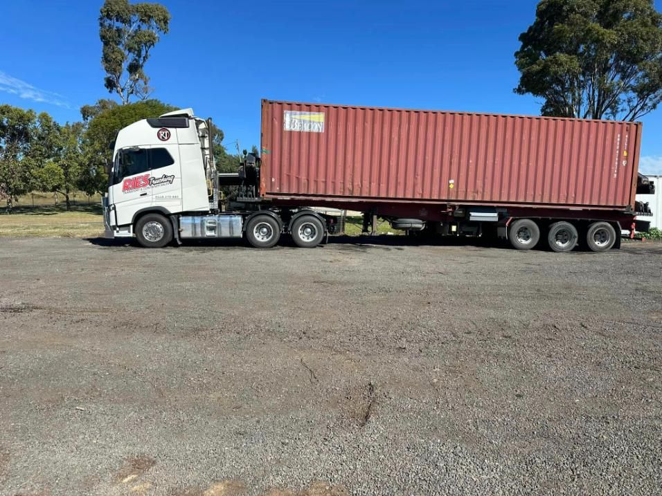 A Semi Truck With A Red Shipping Container On The Back Is Parked In A Gravel Lot — Ries Trucking in Chinchilla, QLD