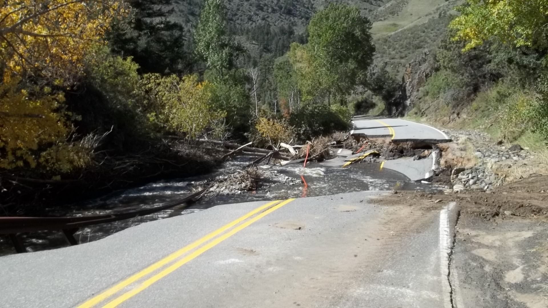 Rural road washed out by landslide, with debris blocking the pavement and broken asphalt