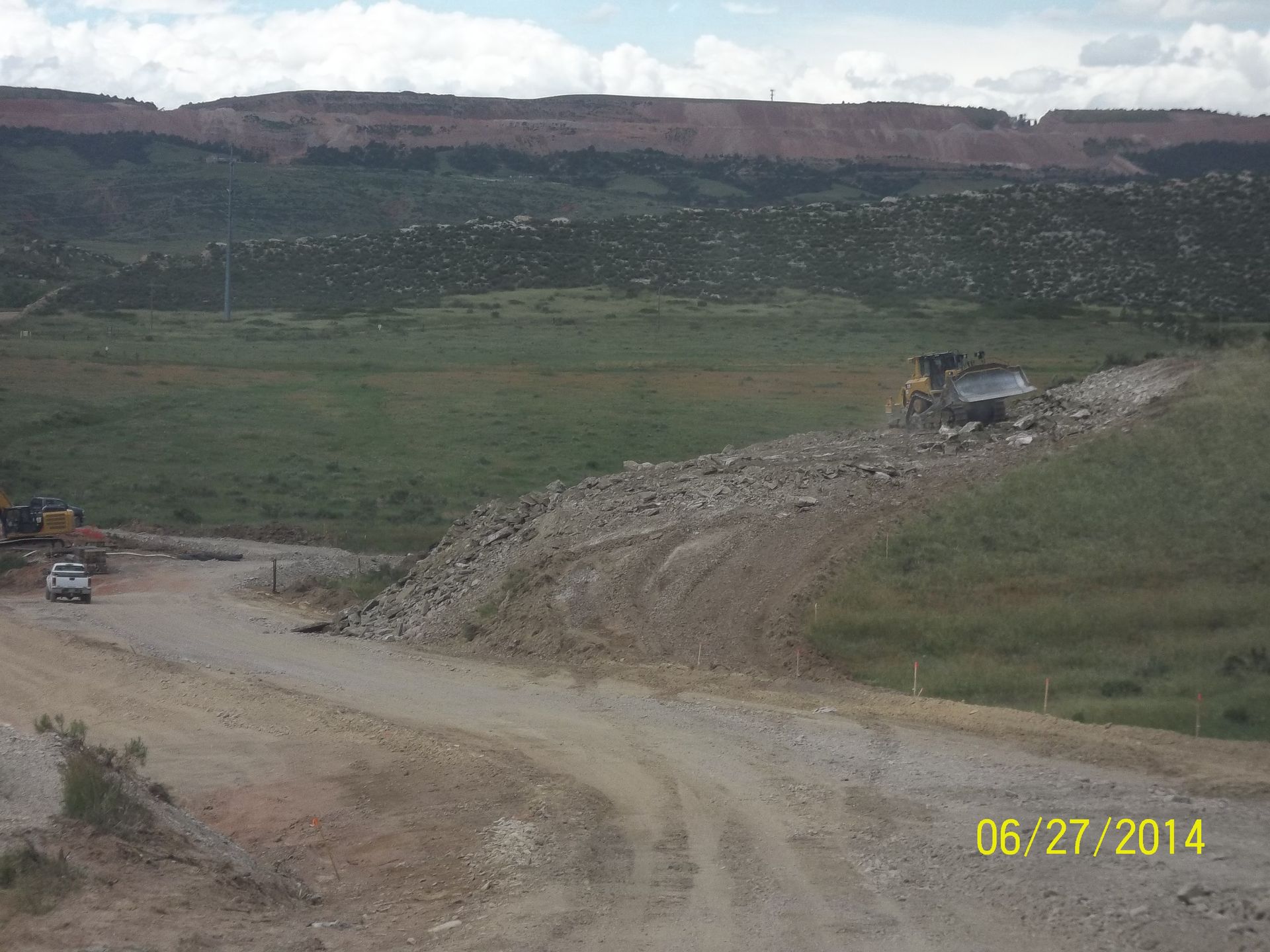 Excavator clearing dirt beside a concrete drainage culvert at a construction site under clear sky