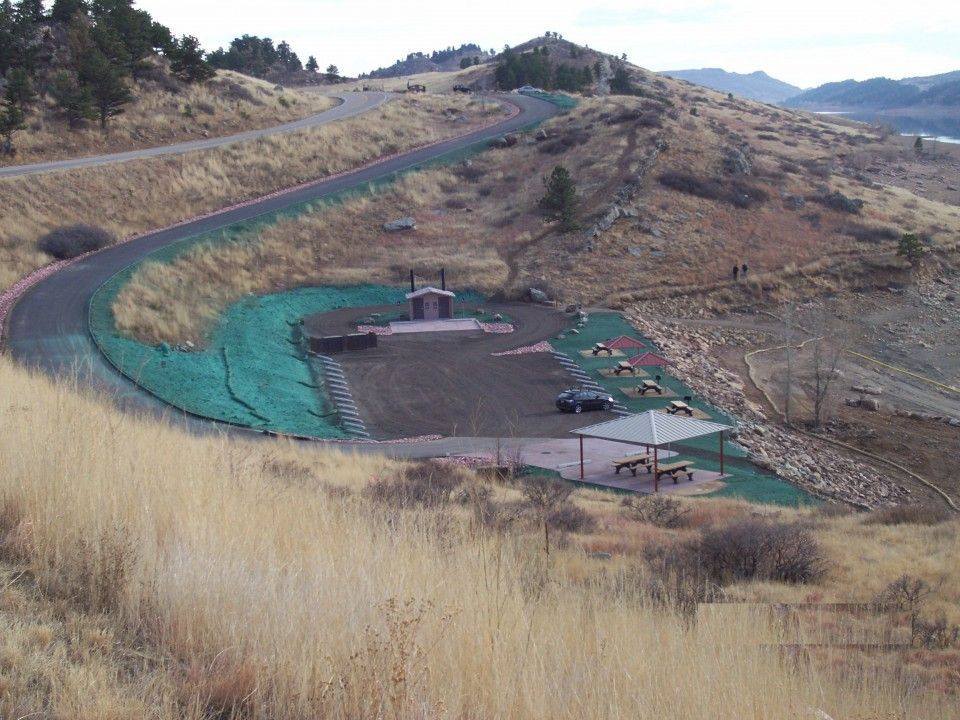 Curved hillside construction site with green erosion netting and a small building at center