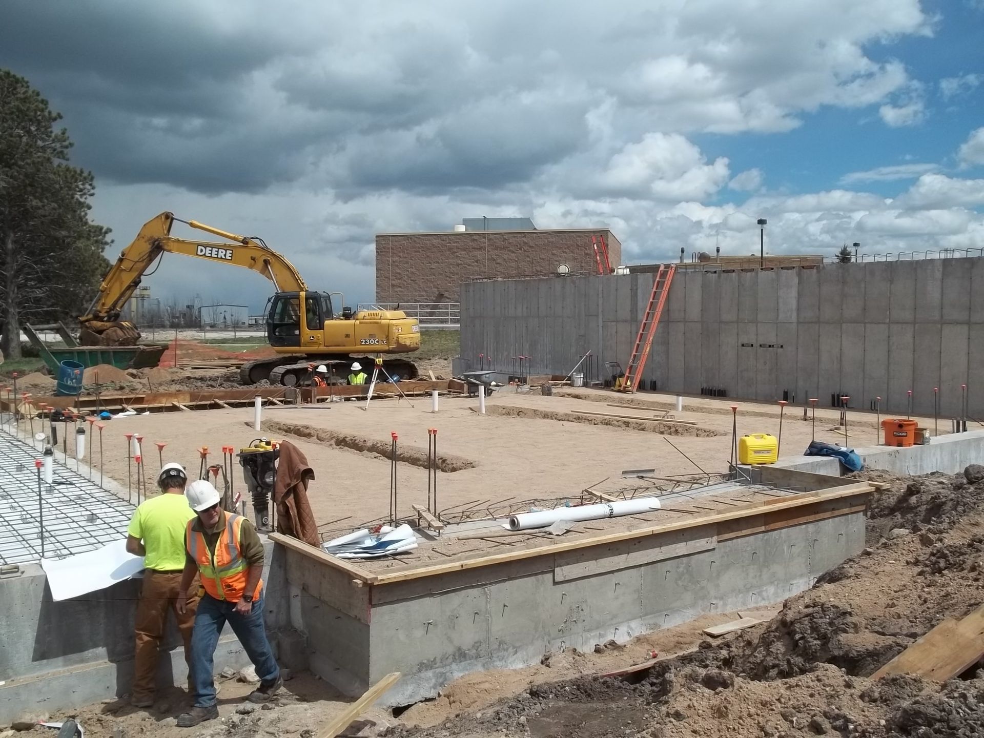 Construction site with excavator, concrete foundation, and workers under cloudy sky