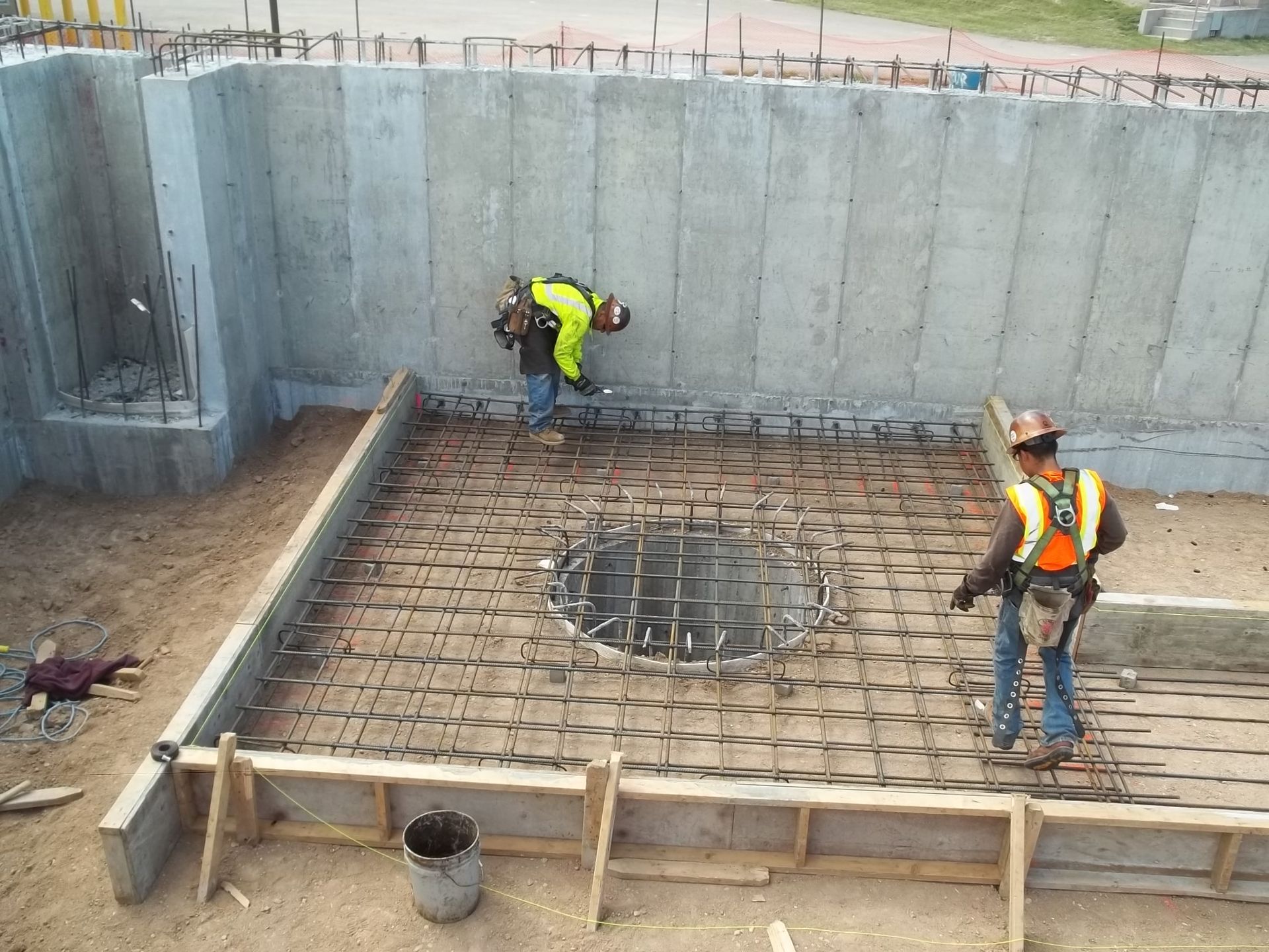 Construction workers installing rebar in a large concrete foundation pit