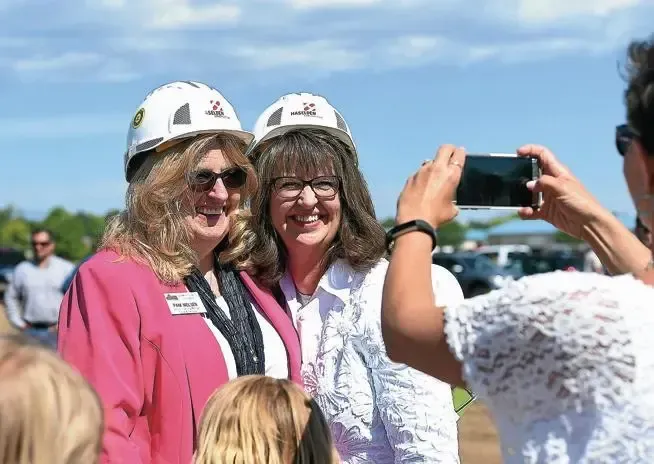 Two smiling people wearing white helmets pose for a photo outdoors while someone takes their picture.