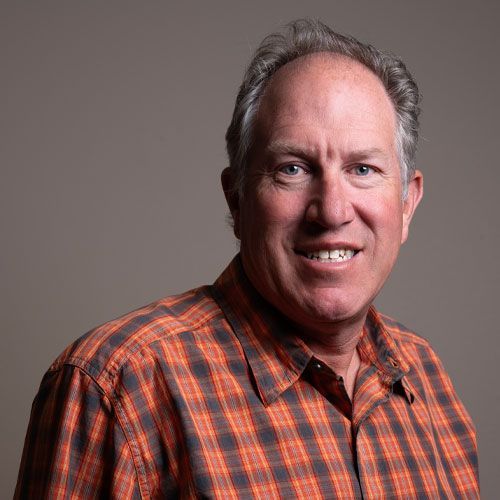 Portrait of a smiling man in an orange plaid shirt against a gray background