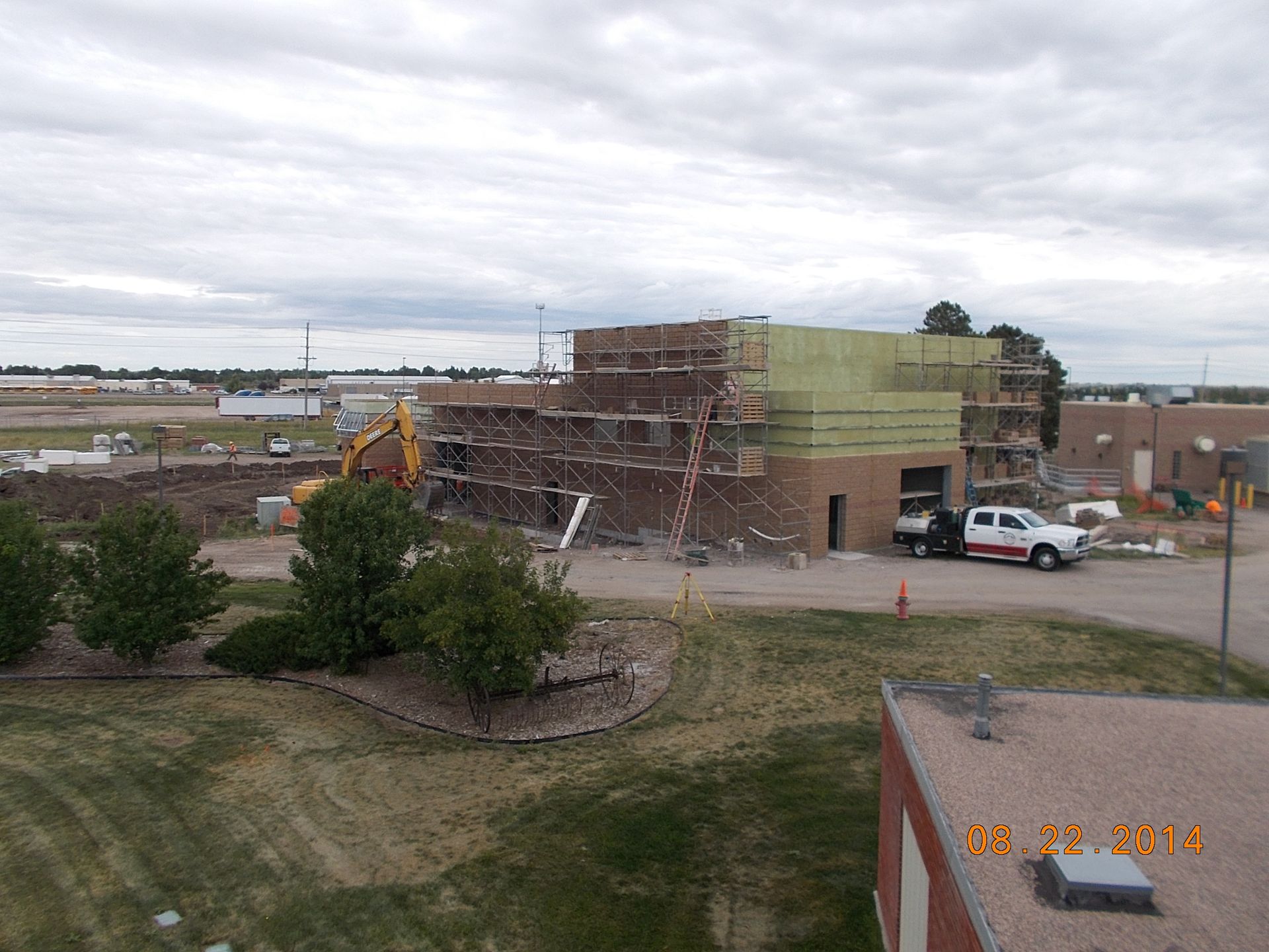 Construction site with a partially demolished brick building, excavator, and white truck under cloudy skies.