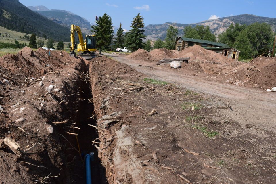 Excavator beside a deep trench at a dirt construction site with mountains in the background