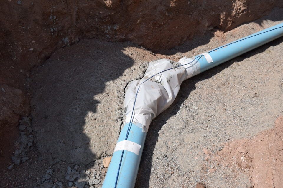 Blue PVC pipe repair wrapped with white tape in a dirt trench
