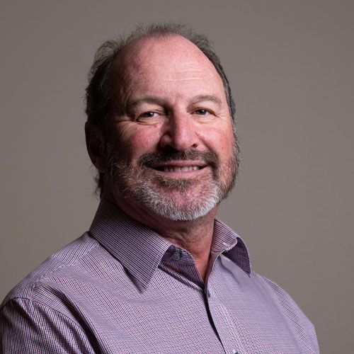 Smiling man in a purple checkered shirt against a gray background