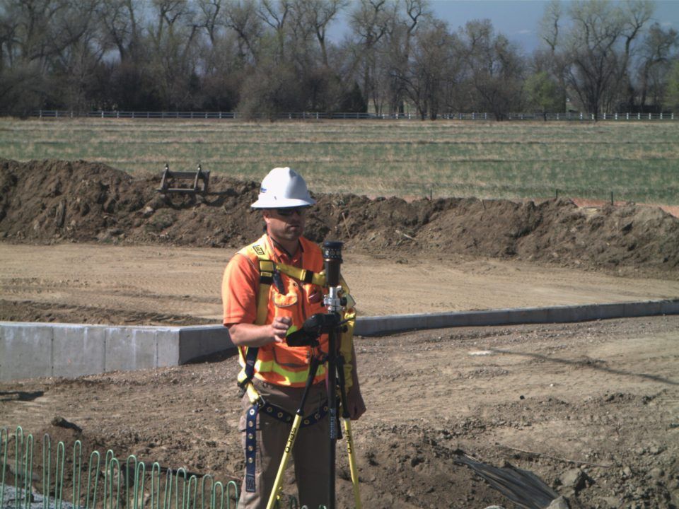 Worker in hard hat and orange vest using surveying equipment on a construction site