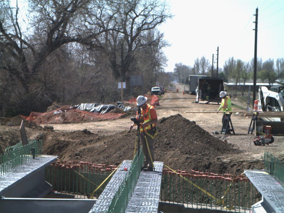 Road construction site with workers, dirt piles, and rebar along a rural roadside