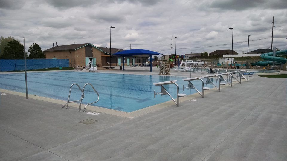 Empty outdoor swimming pool with metal handrails and a gray deck under cloudy skies