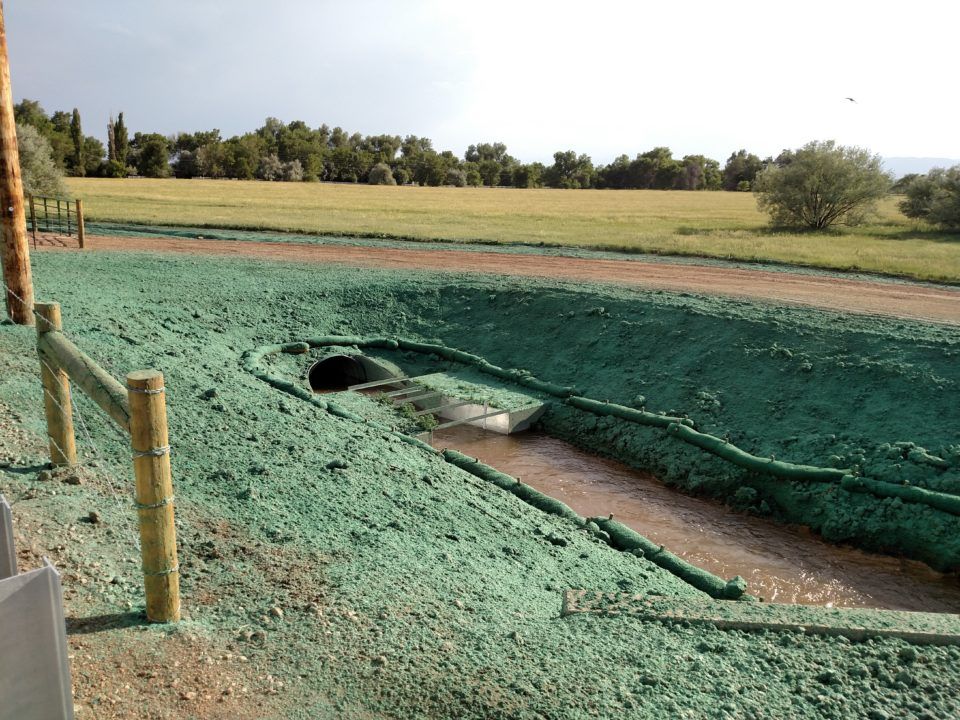 Green-lined water trench with a pipe opening and dirt path in a grassy field
