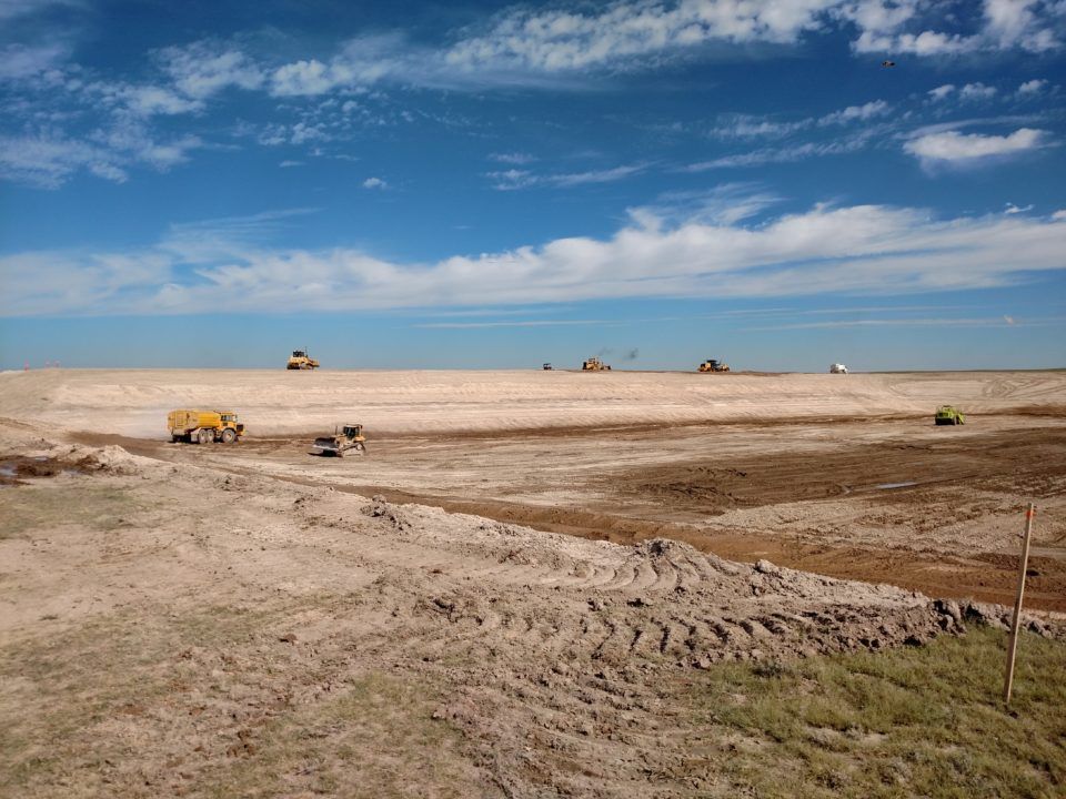 Bulldozers working on a vast dry construction site under a blue sky with clouds