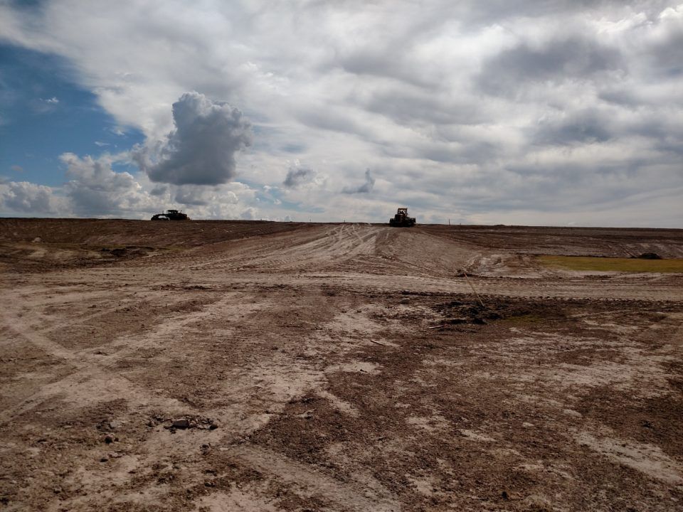 Dirt road crossing a barren field under a cloudy sky