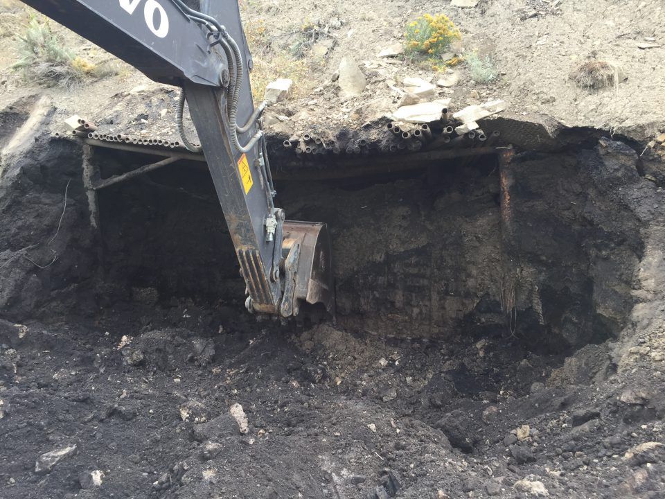 Excavator digging into a dark soil pit on a rocky hillside