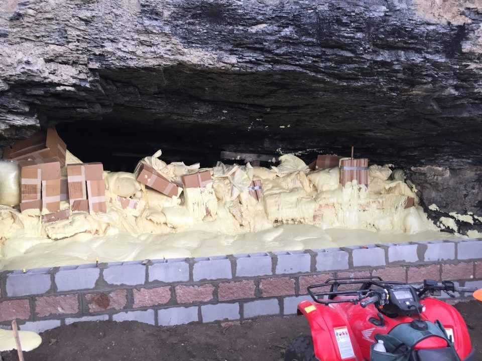 Brick hearth with stacked firewood under a rocky overhang, with a red ATV in front