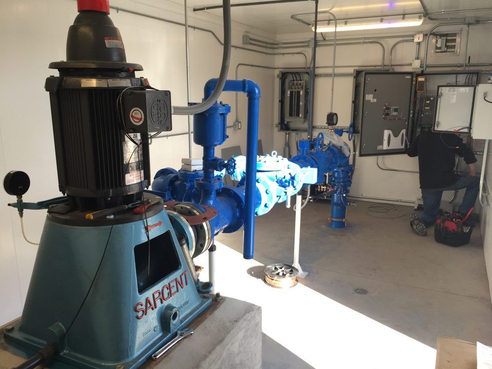 Industrial workshop with large blue machinery, pipes, and bright sunlight streaming across the floor