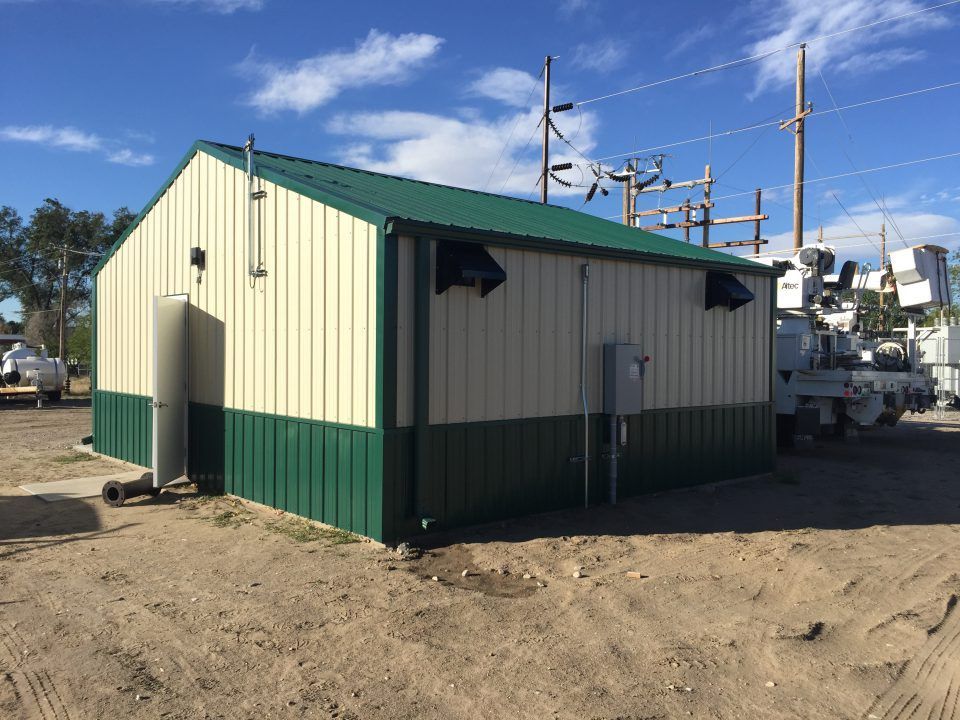 Small green-and-beige utility shed on a dirt lot near boats and marina equipment