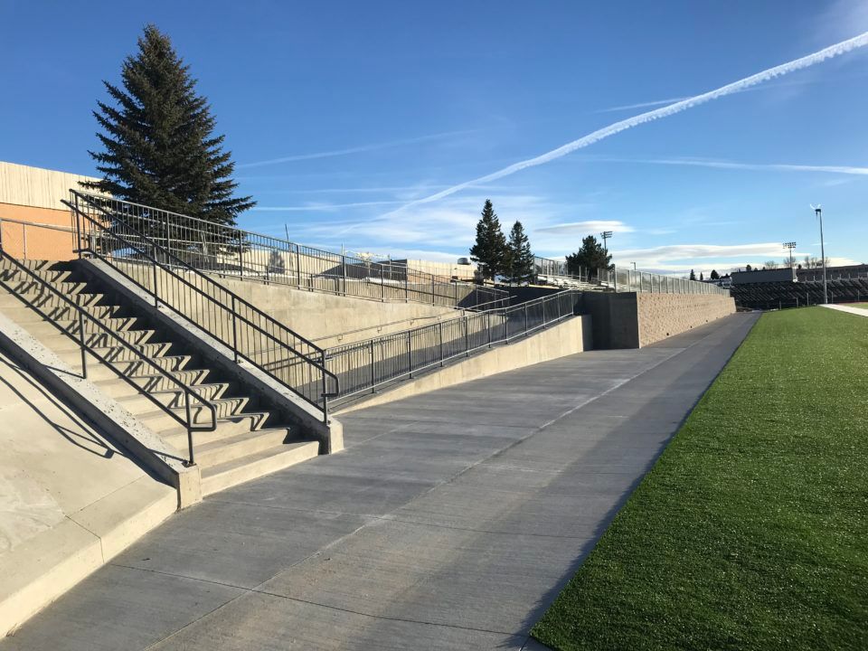 Outdoor walkway with concrete stairs, railings, and a grassy field under a clear blue sky