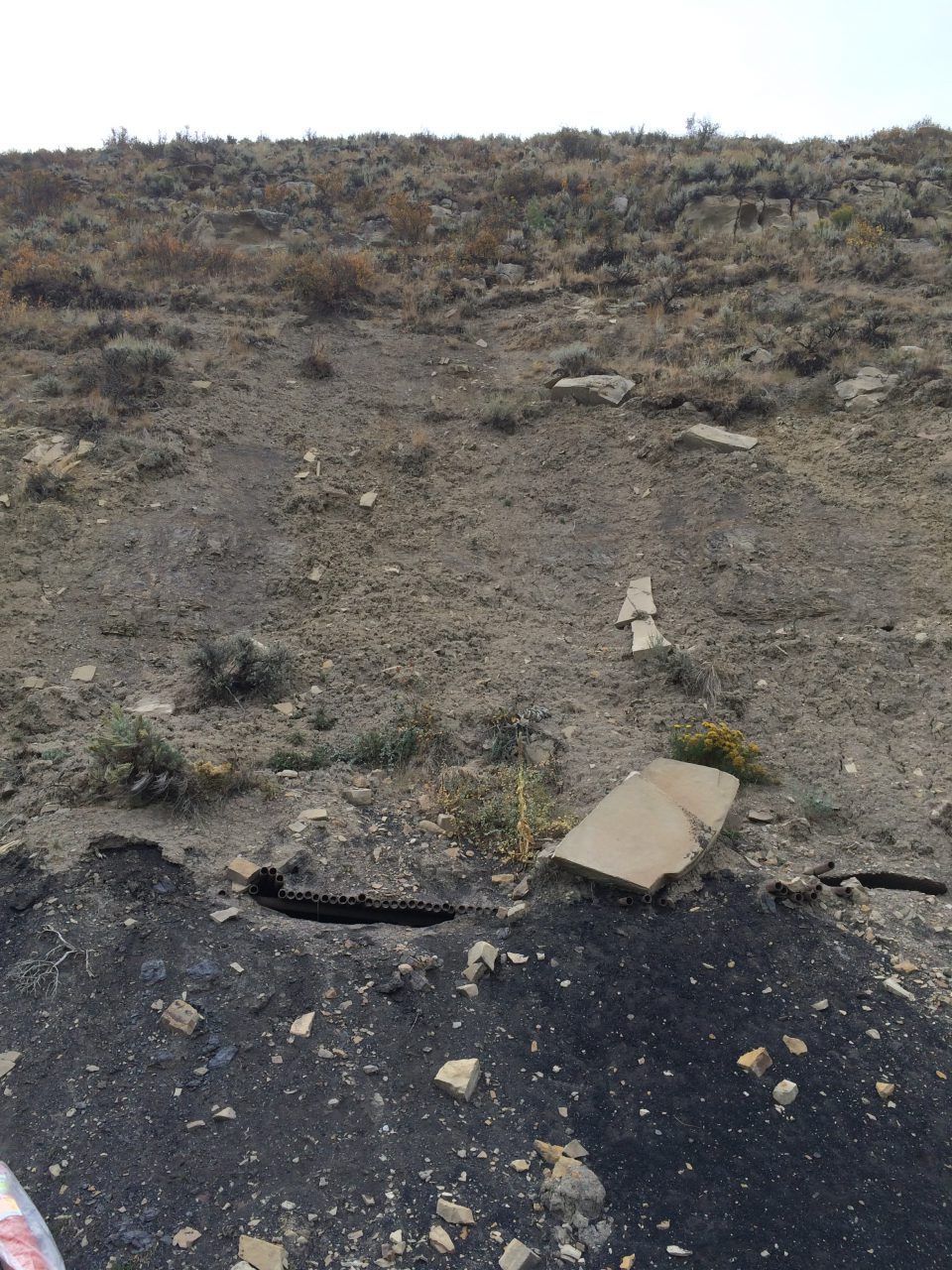 Rocky dirt embankment beside a cracked asphalt road with scattered debris and sparse dry grass.