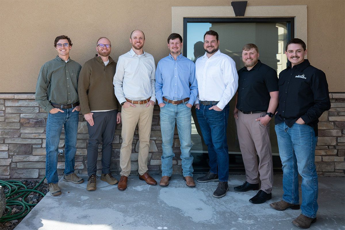 Seven people standing shoulder to shoulder outside a building, posing for a group photo.