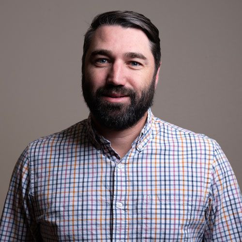 Smiling man in a plaid shirt against a gray background