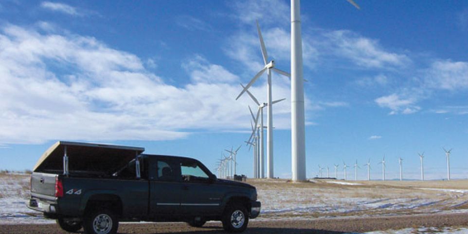 Black pickup truck beside wind turbines in a snowy field under a blue sky