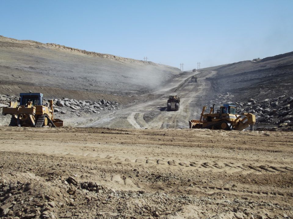 Bulldozers and dump trucks working in a dusty open-pit mine on a rocky hillside