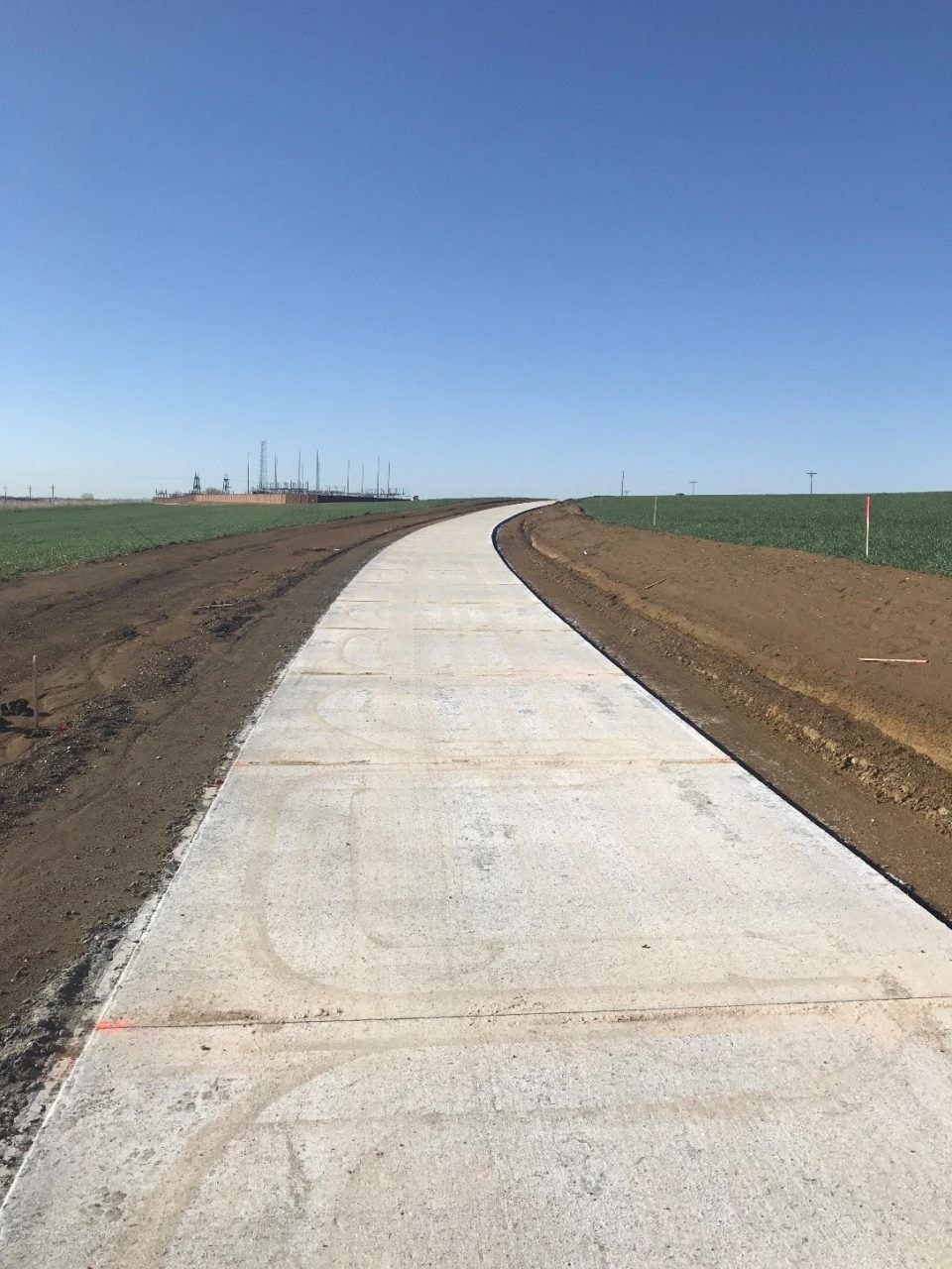 Concrete path through open fields under a clear blue sky