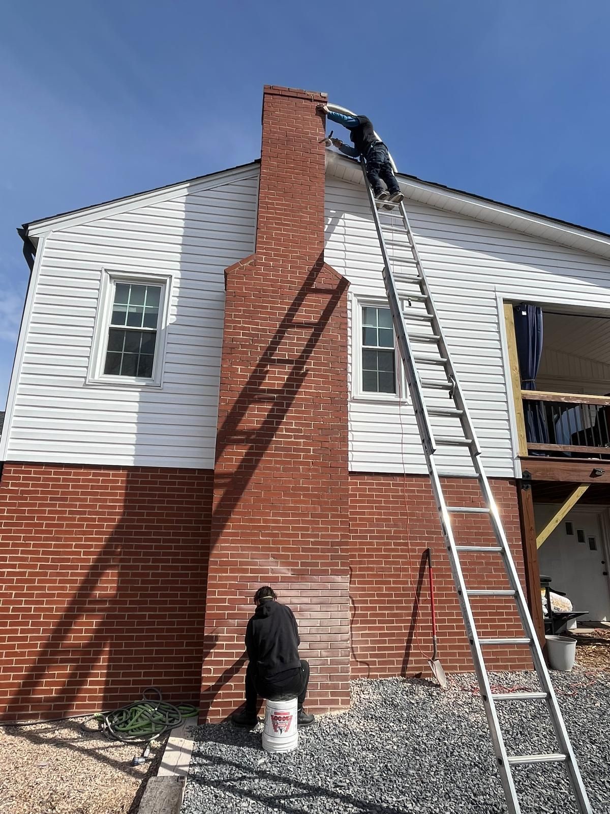 Worker on a ladder repairing a brick chimney on a white and red house.
