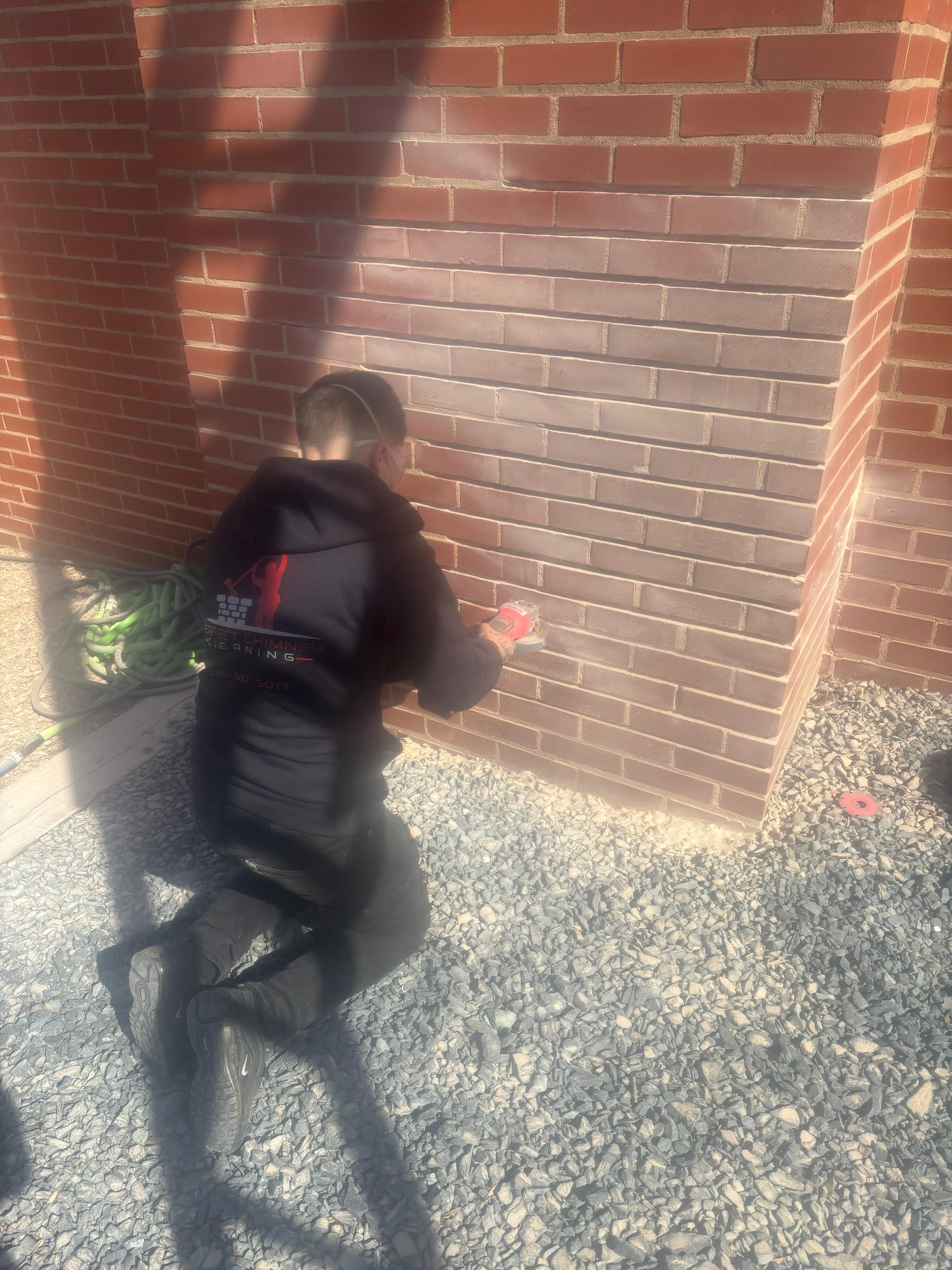 Child crouching by a red brick wall, wearing a black outfit in bright sunlight.