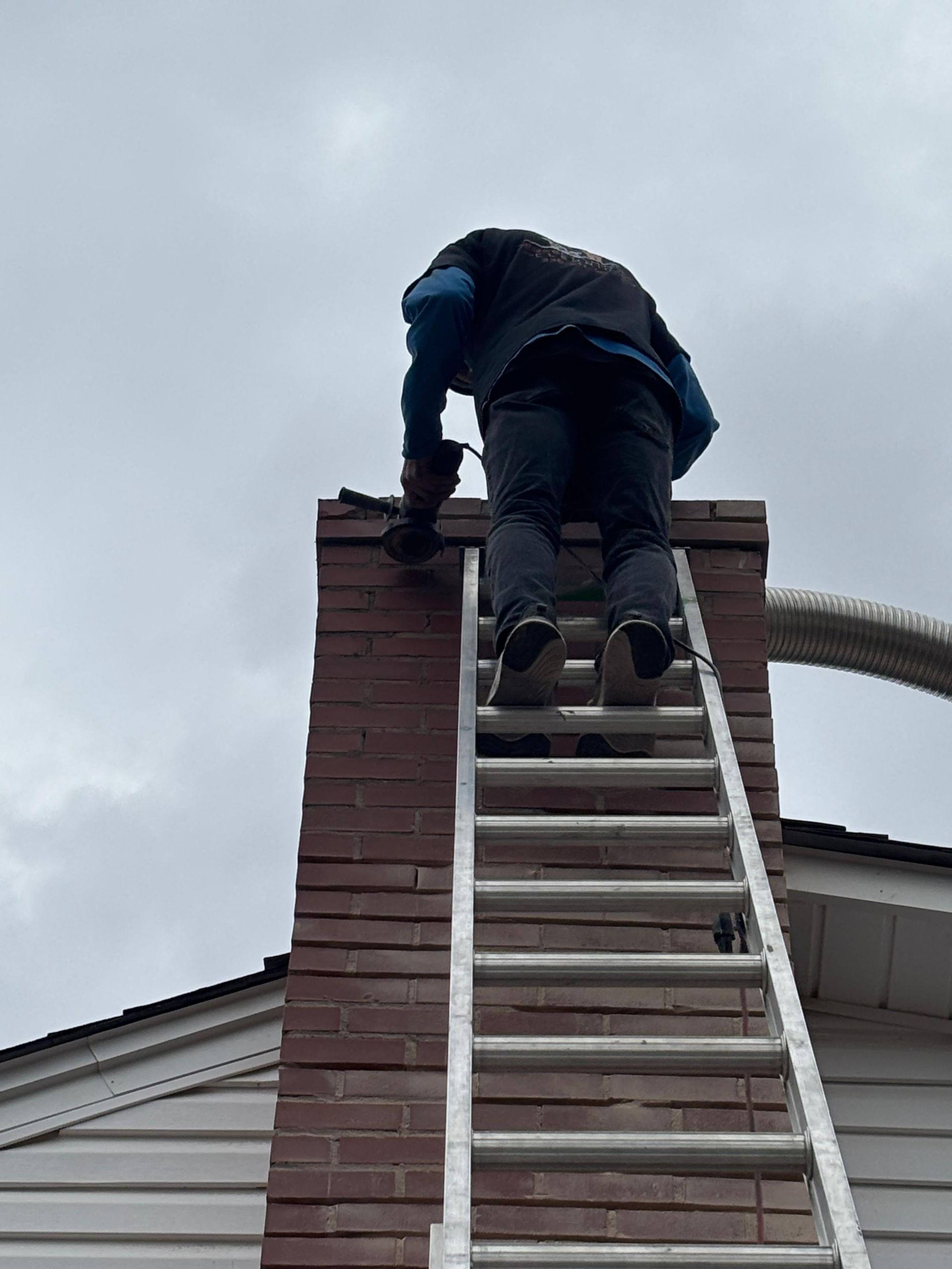 Worker on a ladder repairing a brick chimney on a house roof