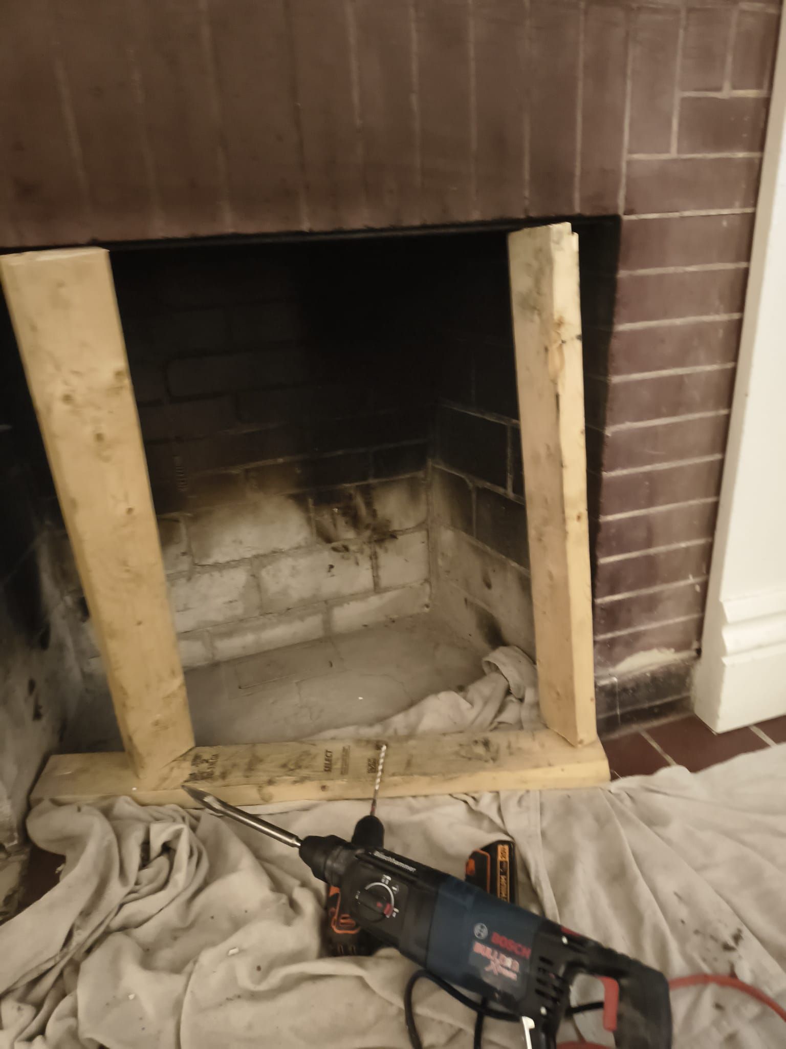 Partially disassembled brick fireplace with power tool and drop cloth on the floor