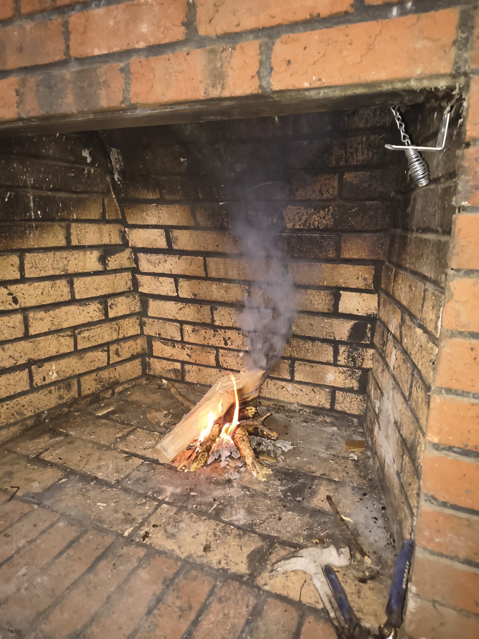 Small fire burning in a brick fireplace, with smoke rising up the chimney.