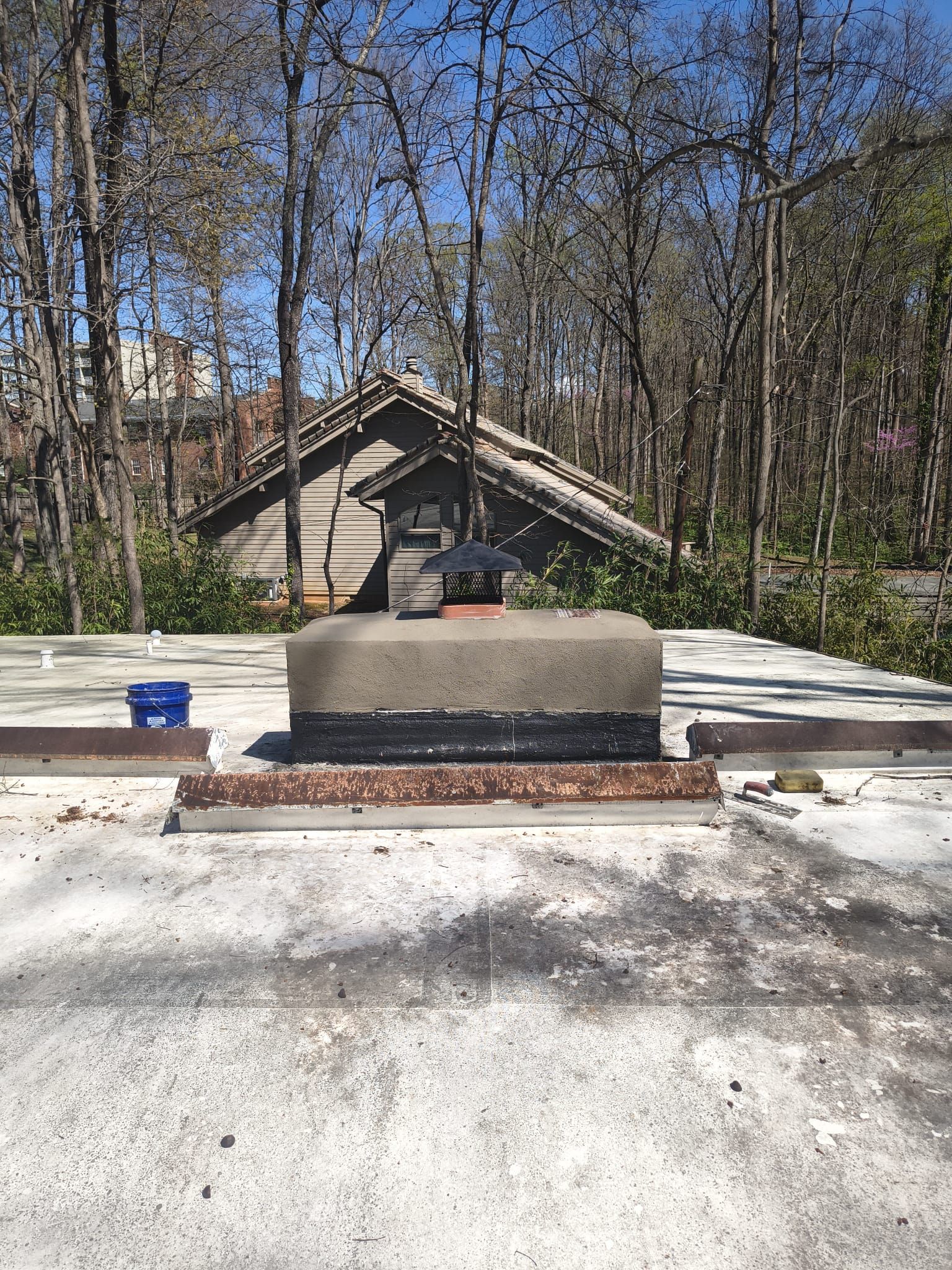 Concrete bench beside a gravel path in a wooded park, with a small shelter in the background.