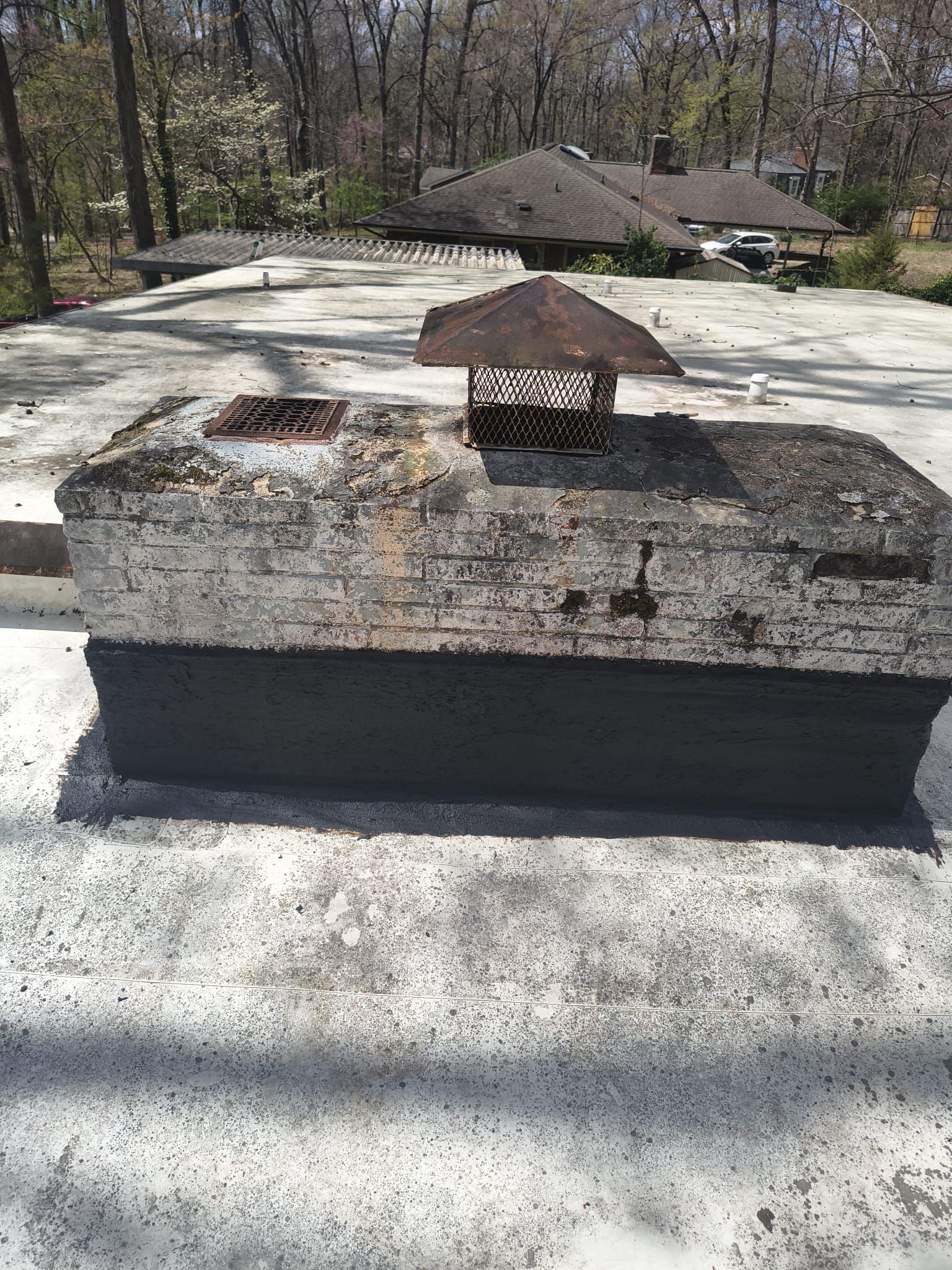 Rusted rooftop vent on a weathered concrete roof, with trees and a house in the background.