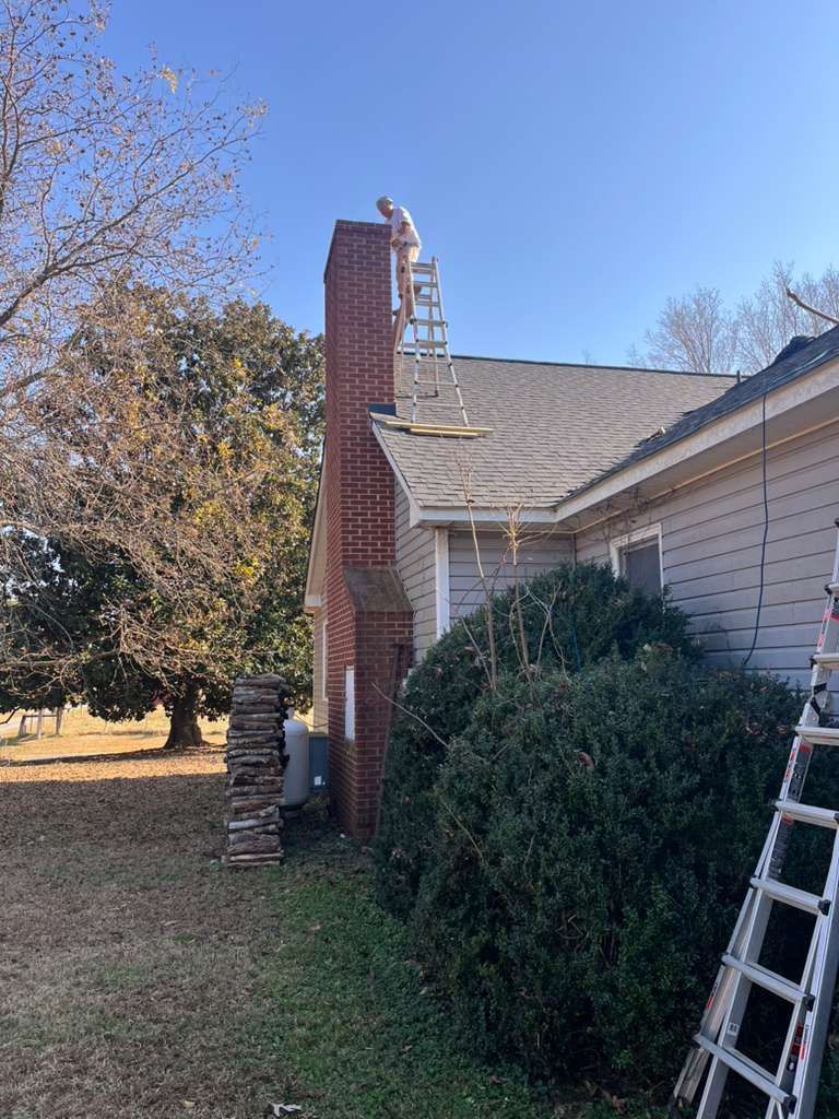 Brick chimney beside a house with a ladder leaning against the roof under a clear blue sky