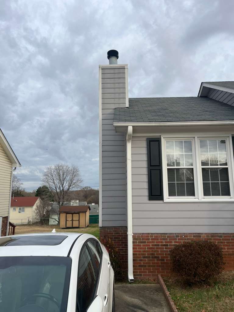 House exterior with a gray chimney, brick and siding, a white car, and cloudy sky