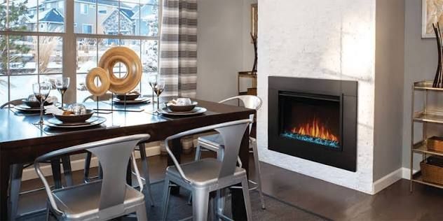 Modern dining room with dark table, silver chairs, large windows, and a white fireplace with a fire burning