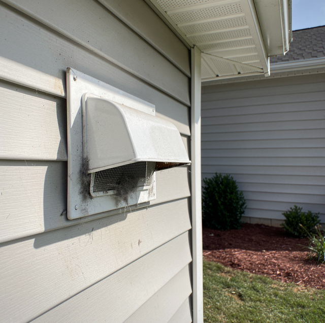 Broken white vent cover on a house exterior wall with visible damage and debris underneath