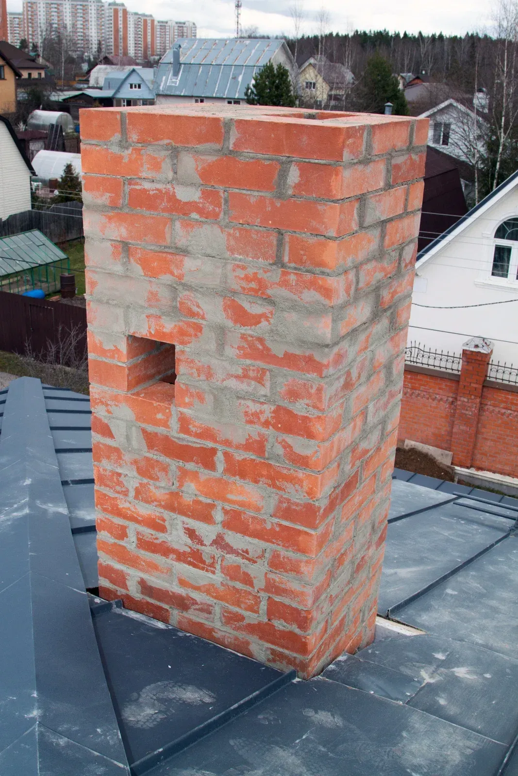 Brick chimney with metal flashing on a gray shingle roof, showing cracked mortar at the base.