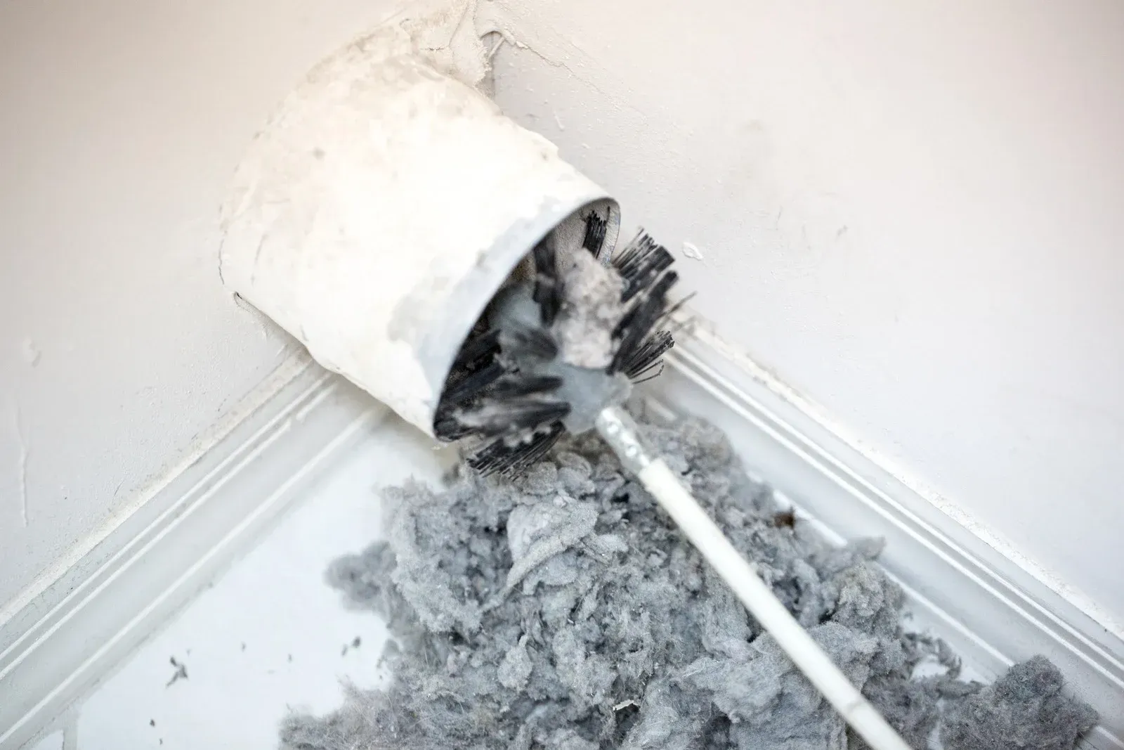 Broken white vent cover on a house exterior wall with visible damage and debris underneath