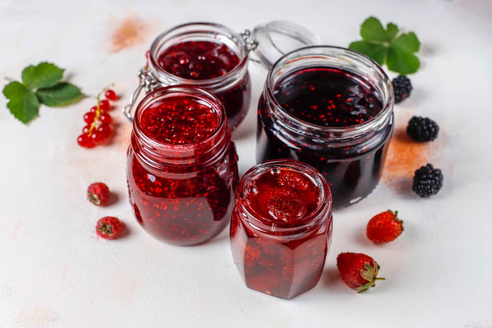 four jars of berry jam are sitting on a table .