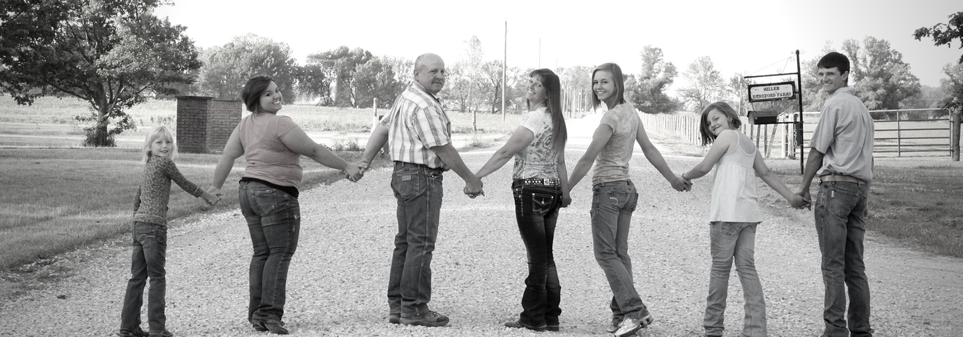 Six people holding hands in a line outdoors in a park, with trees and grass in the background.